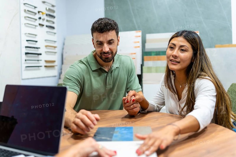 Smiling young couple collaborating with a sales consultant, discussing samples and making decisions for their home improvement project at a modern showroom, focusing on new design options