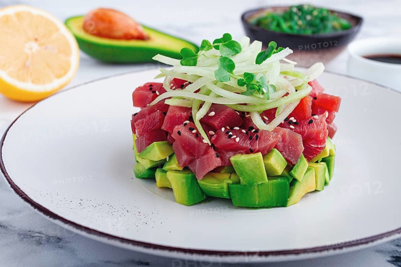 Fresh tuna tartare with avocado served on a marble table with soy sauce and seaweed salad