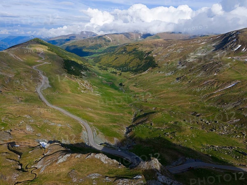 Winding road through green mountain valley under a sky full of clouds, aerial view, near Rânca, Ranca, Transalpina high road, Drum na?ional 67C, national road, Transylvania Alps, South Carpathians, Romania