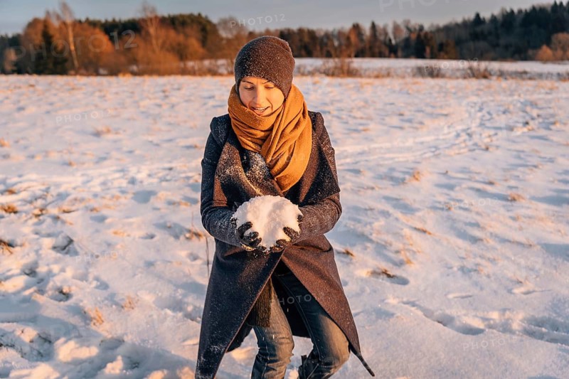 A woman in winter clothes collects a lump of snow in a snow-covered field