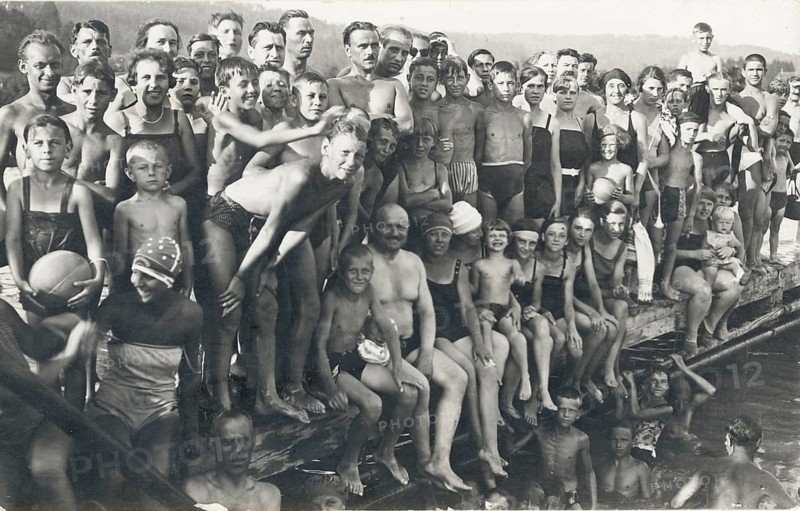 Outdoor pool, bathing, summer, leisure, a multitude of people of all ages standing and sitting close together at the edge of a river, around 1928