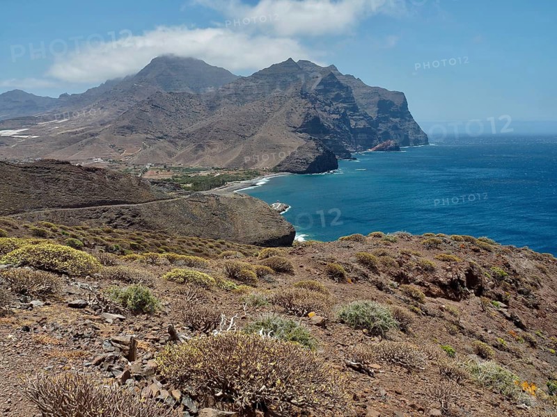 Rugged coastal landscape with hills and views of the blue sea under slightly cloudy sky, La Aldea de San Nicolas, Gran Canaria, Spain