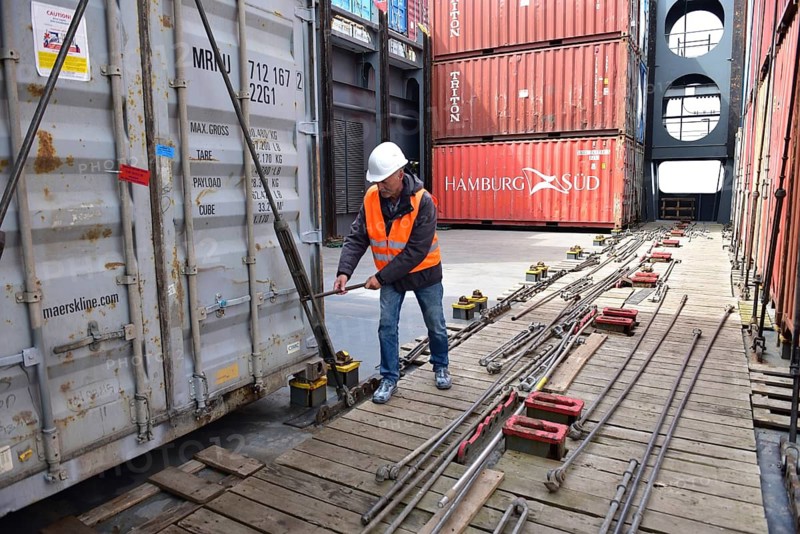 In the port, a man with safety equipment works on stacks of containers on a wooden platform, workers on the tie rods on a container ship, Schleswig-Holstein, Germany