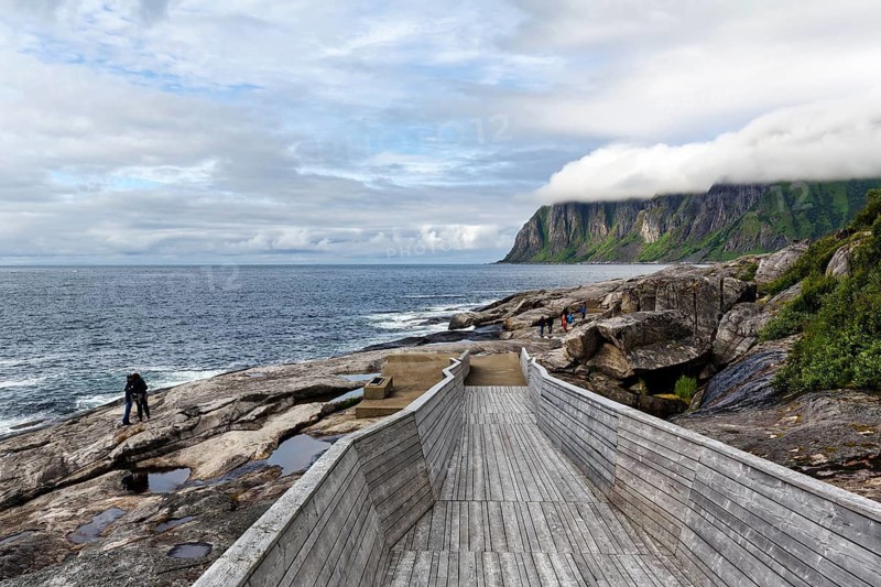 Tungeneset viewpoint, rest area, wooden walkway to the sea, hiker, rocky coast, Okshornan mountain range, Norwegian Senja landscape route, cloud cover, Norway