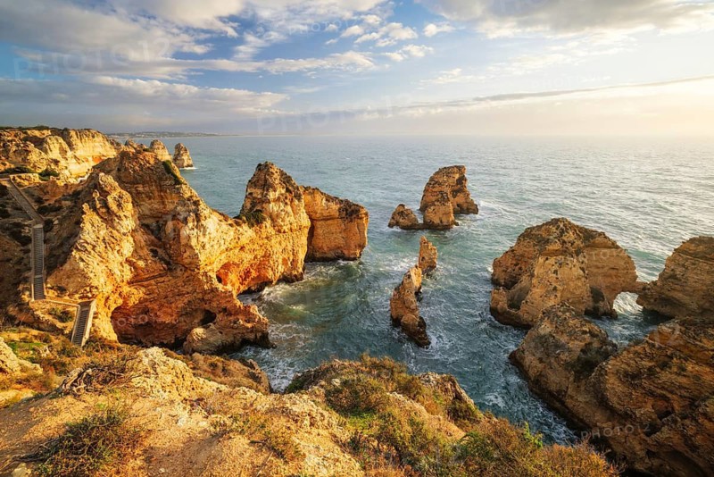 Calm sunrise view of Ponte da Piedade in Lagos, Algarve, Portugal, with ocean cliffs, sea stacks, Atlantic water, and warm sky