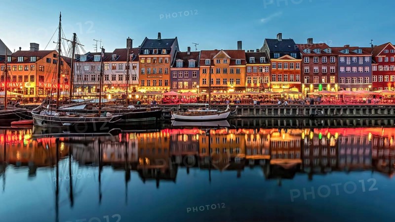 Abend am Hafen mit beleuchteten, bunten Gebäuden und ruhig liegenden Booten, Kopenhagen, Dänemark, Nyhavn
