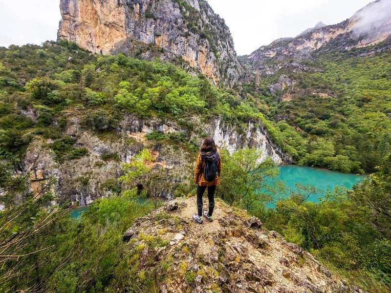Woman standing on a rocky outcrop overlooking the turquoise waters of the cinca river, surrounded by lush green mountains and dramatic canyon walls in entremon gorge, huesca, spain