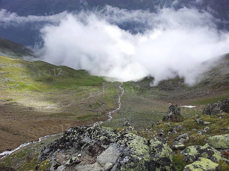 View of a valley with flowing clouds surrounded by mountains and green meadows, E5, hiking in the Alps, crossing the Alps, Austria