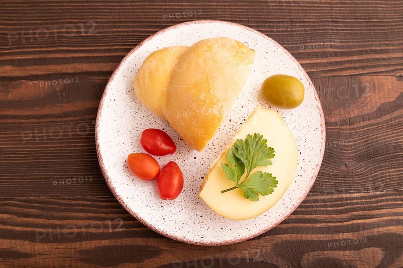 Smoked Mozzarella cheese, with tomatoes and olives on brown wooden background, top view, flat lay, copy space
