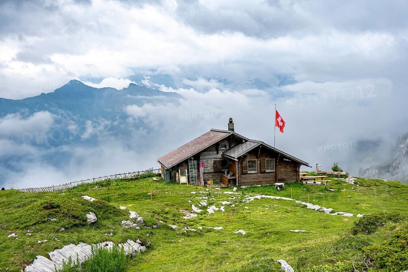 Small mountain hut Suls-Lobhornhütte with Swiss flag, cloudy mountain landscape, Bernese Alps, Bernese Oberland, Switzerland