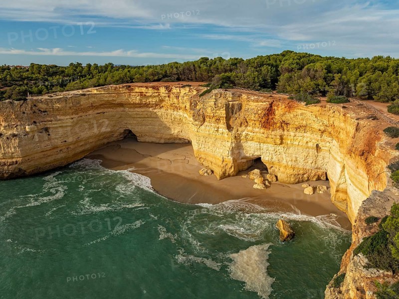 Drone view of cliffs above Benagil Cave in Algarve, Portugal, with a sandy cove, limestone rock walls, Atlantic waves, and turquoise water