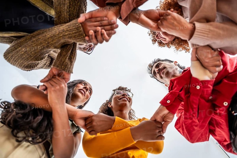 Diverse group standing in a circle, holding wrists and looking up with smiles, conveying unity, trust, support, community, collaboration, and shared well being