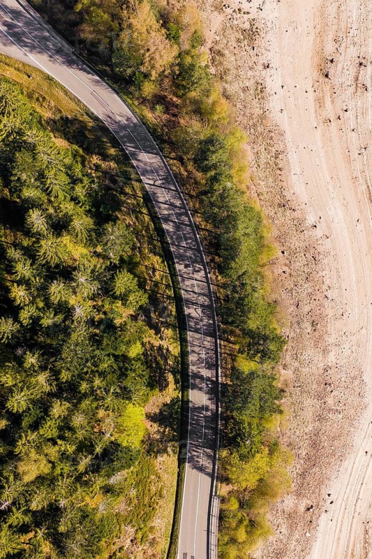 Winding road in a wooded area along dry soil from a bird's eye view, emptied Schwarzenbach Reservoir, Forbach, Black Forest, Germany