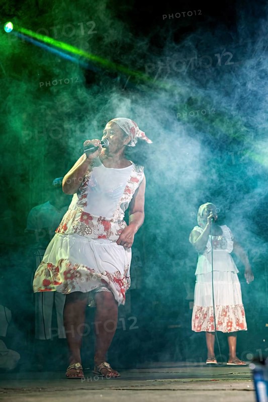 Singer in traditional dress sings with green lighting effects and fog, a band plays and dances at a festival in Petrolina in Brazil