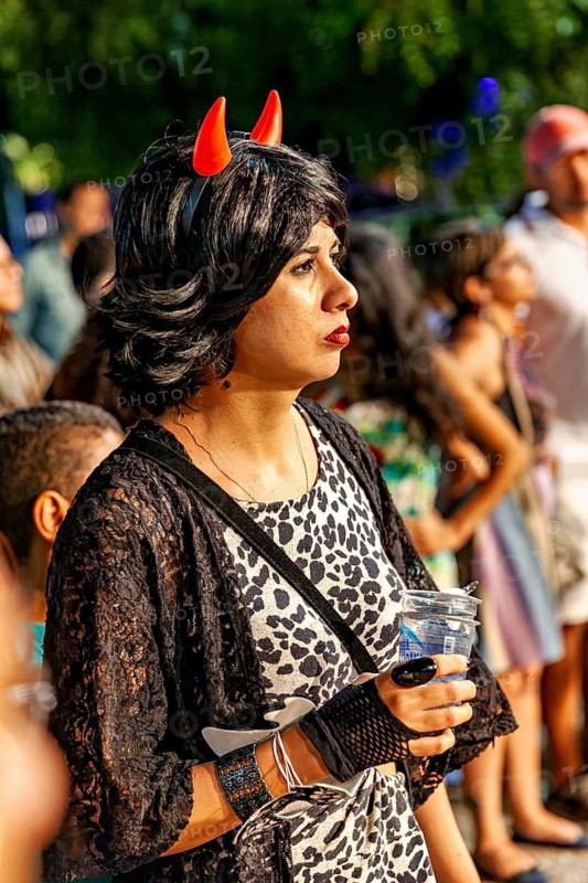 Woman with small horns on wig looks interested in one direction at night, visitor to a festival in Petrolina Brazil