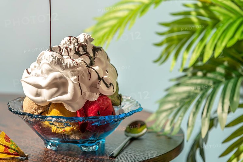 Sundae decorated with cream and chocolate next to green leaves