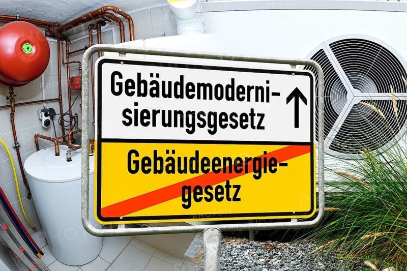 Town sign with the inscription Building Modernization Act and crossed out inscription Building Energy Act in front of gas heating and heat pump, photo montage +++ editorial use only