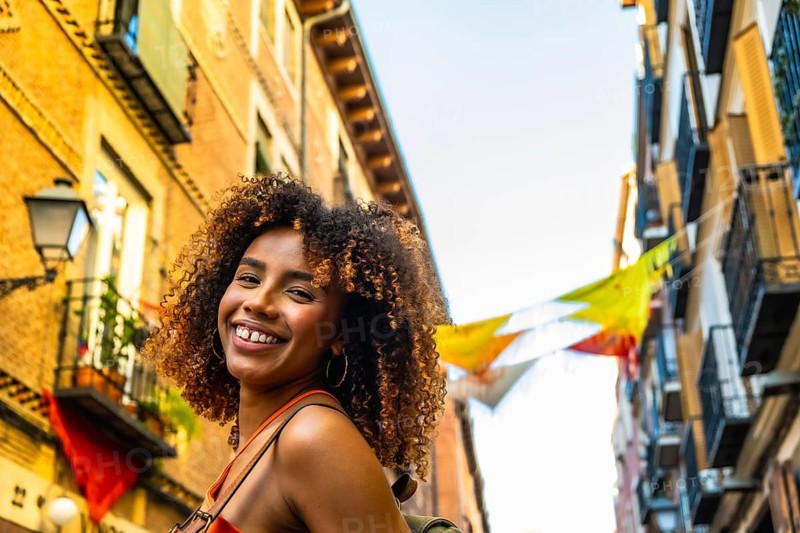 Happy black woman with afro hair smiling while walking through a colorful street in madrid, enjoying urban travel and exploration during golden hour at sunset