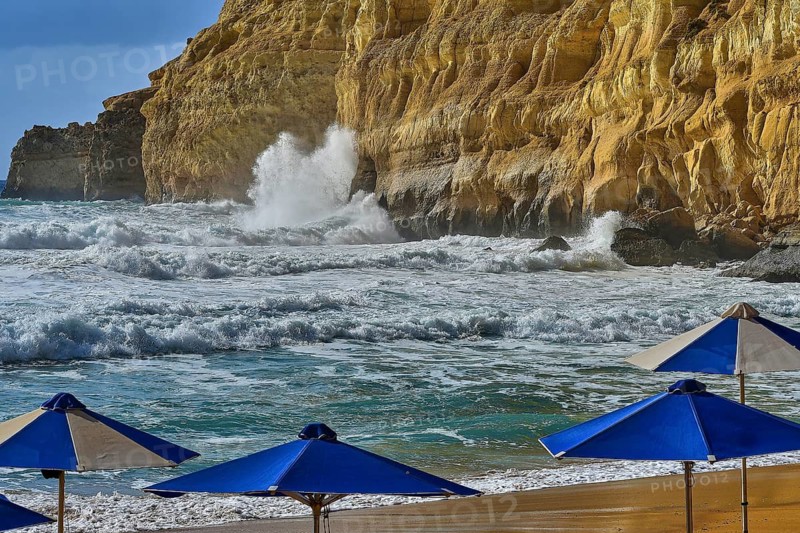 Red Beach, a dream beach in the neighboring bay of Matala, beach with blue umbrellas against rocky coast and rising waves, Matala, south coast, Crete, Greek Islands, Greece
