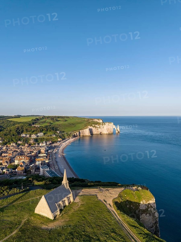 Aerial view of the Notre Dame de la Garde chapel after sunrise at the Falaise d'Amont viewpoint, on the right the coastal town of Étretat with the beach, on the horizon the Porte d'Aval rock formation, Étretat, Alabaster Coast, La Côte d'Albâtre, chalk cliffs, English Channel, Seine-Maritime, Normandy, France