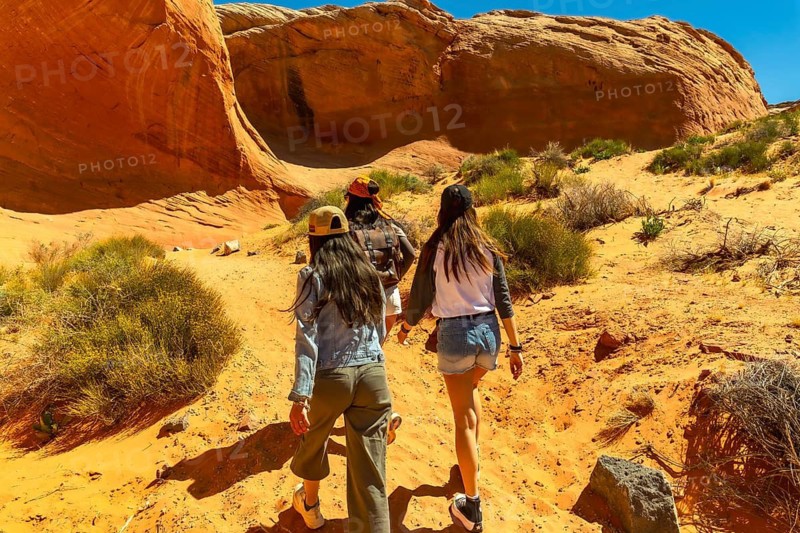 Three friends exploring the arid landscape and rock formations, walking along a sandy desert trail toward the magnificent biidi the arch cave near page, arizona, enjoying their outdoor adventure