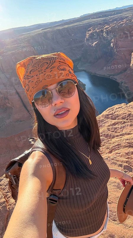 Young woman in bandana and sunglasses stands on sandstone cliff at horseshoe bend, overlooking the winding colorado river adventurous travel, scenic canyon vista, sunny day
