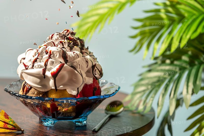 Sprinkles fall on sundaes decorated with cream and chocolate next to green leaves
