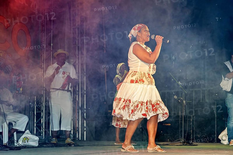 Woman in traditional clothing style sings with fog effects on a stage, a band plays and dances at a festival in Petrolina in Brazil