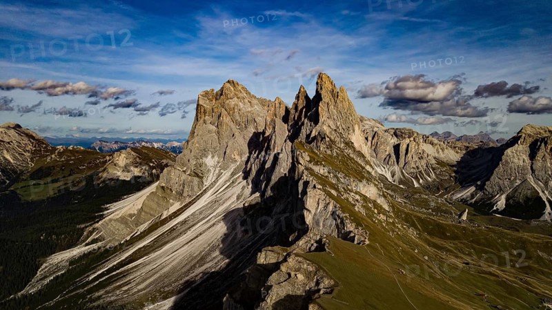 Majestic mountain landscape with dramatic rocks under blue skies and clouds, hiking trails wind their way through lush green valleys under the majestic peaks of the Seceda Mountains in the Italian Dolomites on a sunny summer day