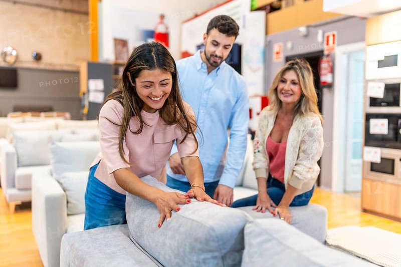 Happy family exploring potential new furniture for their home, touching and testing a grey sofa in a modern showroom while shopping for home improvements