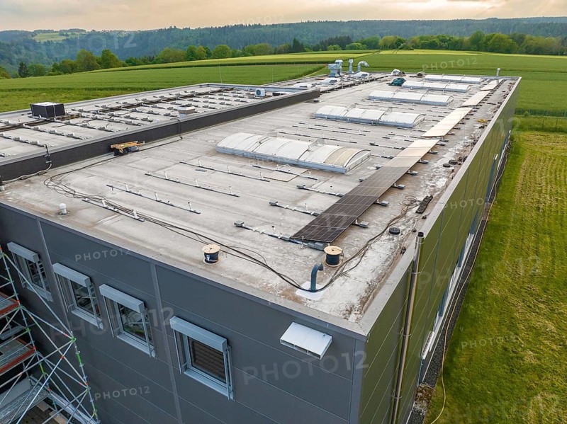 Industrial building with solar panels on the roof, surrounded by green fields, PV assembly, Perrot company, Calw, Germany
