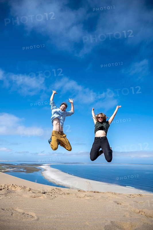 Tourists, young couple jumping in the air, stretching arms in the air, view of high dunes of the Namib Desert on the Atlantic coast, Sandwich Harbour, Namib Naukluft Park, Namib Desert, Namibia