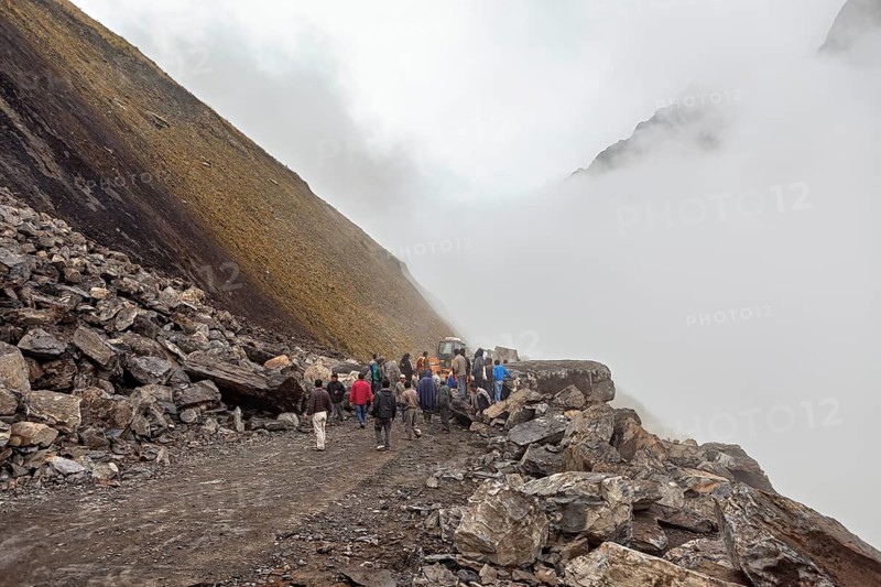 People gather on a foggy, rocky mountain road with a tractor in the background, rockslide on the pass road towards Rurrenabaque through the Andes on the Road of Death in Bolivia