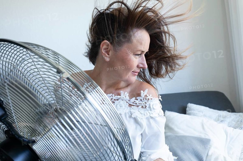 Woman relaxing in front of an electric fan during hot weather at home. during hot weather at home