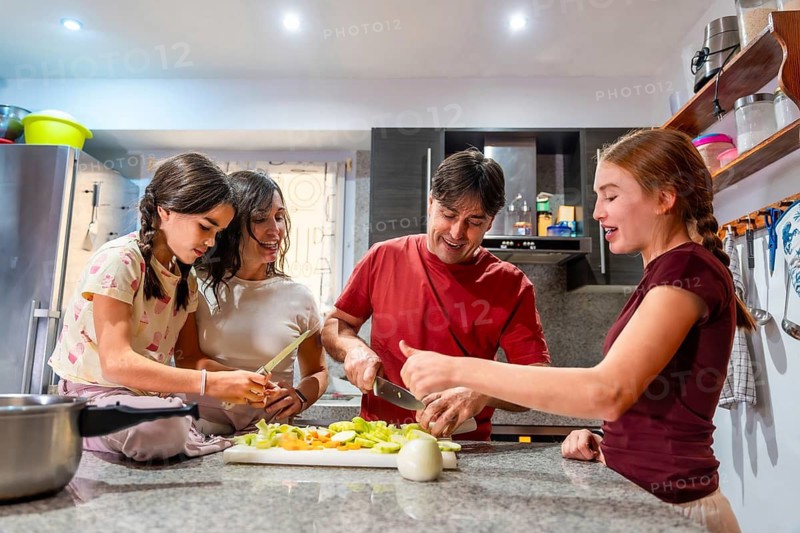 Parents and their two daughters are sharing a happy moment preparing a healthy meal, slicing and chopping ingredients on a cutting board in a domestic kitchen