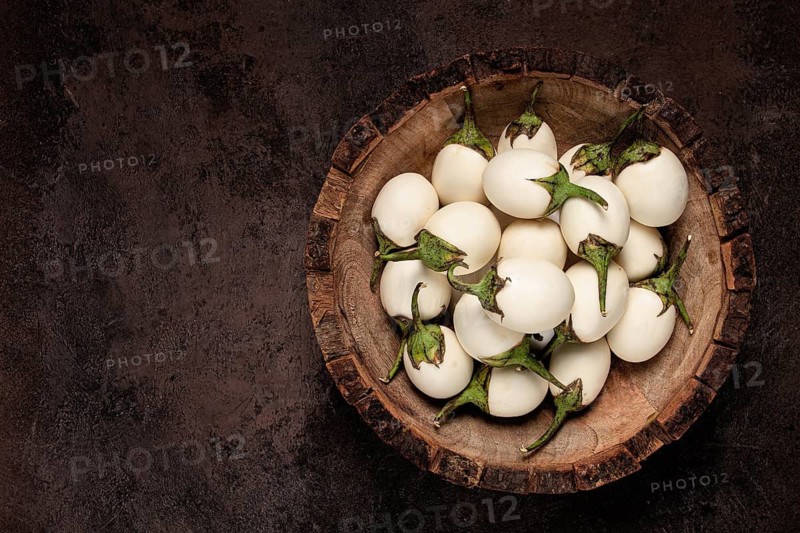 White mini eggplant, in a wooden bowl, on the table, close-up