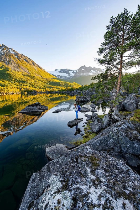 Young woman enjoying the picturesque mountain landscape in the Innerdalen high valley, mountain peaks are reflected in Lake Innerdalsvatna, in the evening light at sunset, Trollheimen Mountain Area, Sunndal, Møre og Romsdal, Norway
