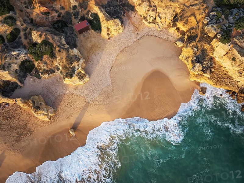 Drone top down view of a sandy cove, foamy surf, and golden cliffs at Praia de Sao Rafael beach