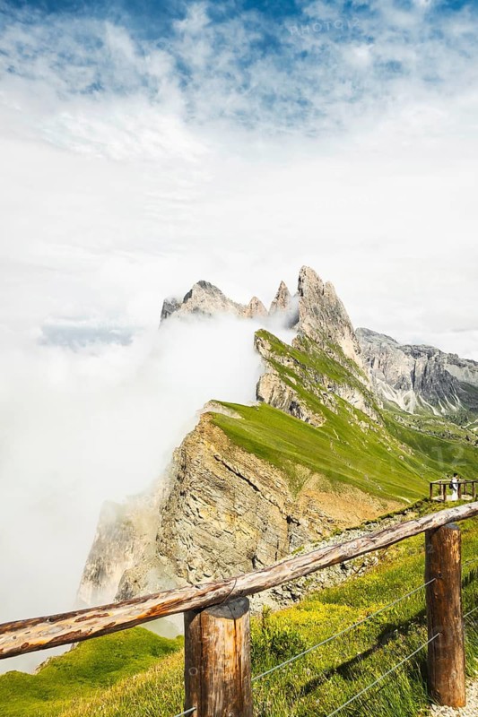 Wooden safety railing fence overlooking dramatic mist covered Seceda mountain peaks steep cliff edge danger zone alpine nature park Dolomites Italy. Minimizing human footprint by protecting vulnerable wildlife