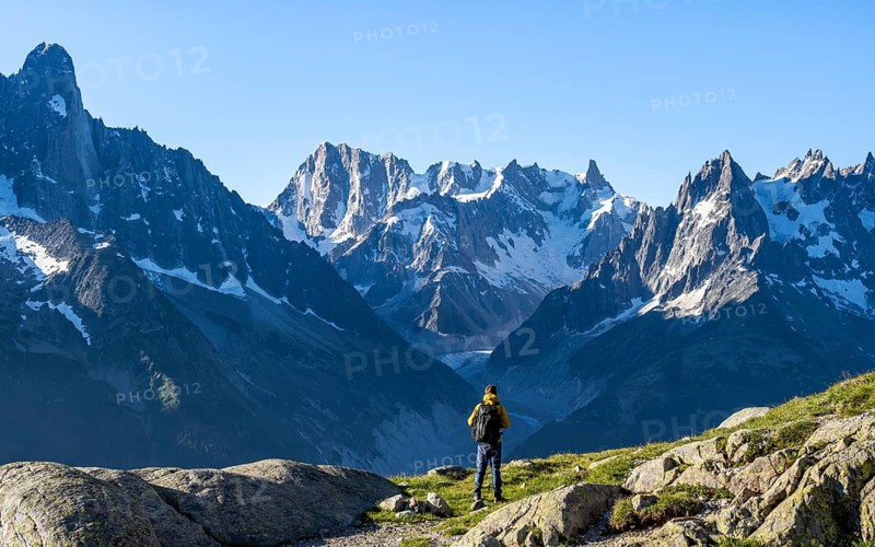 Young man in front of impressive mountain landscape in morning light, picturesque mountain landscape with imposing mountain peaks and glaciers, Mer de Glace glacier, Grandes Jorasses in the background, Mont Blanc Massif, Chamonix-Mont-Blanc, Haute-Savoie, France
