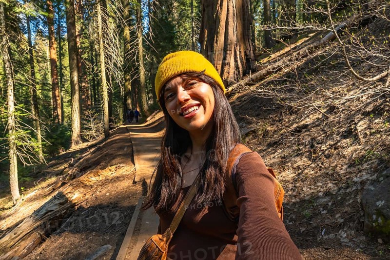 Smiling woman takes a selfie on a sunlit trail through towering redwoods in sequoia national park, enjoying a peaceful hiking escape among giant trees and lush forest scenery