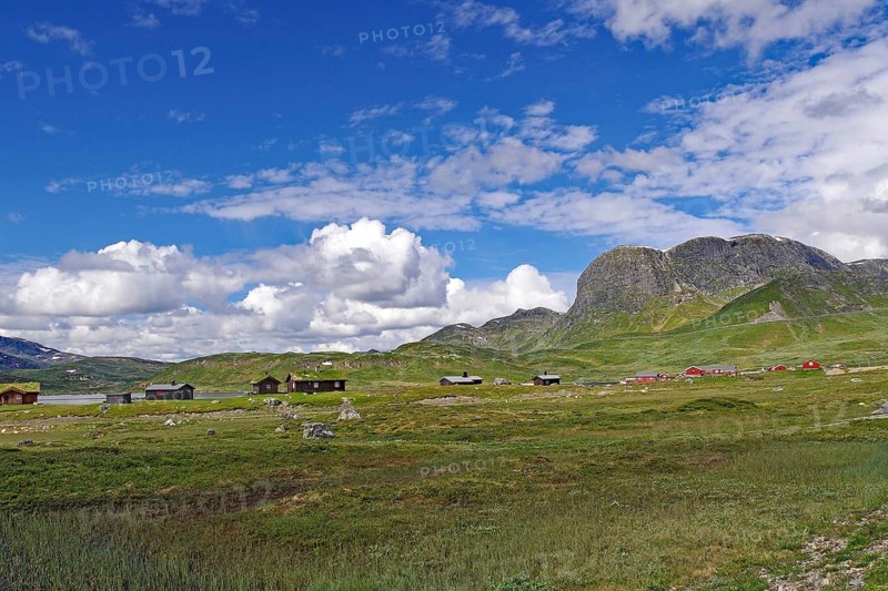 Small settlement of huts on an open meadow, surrounded by mountains and blue skies, alpine pasture, bicycle route, Jotunheimvegen, Mjolkeveien, Norway