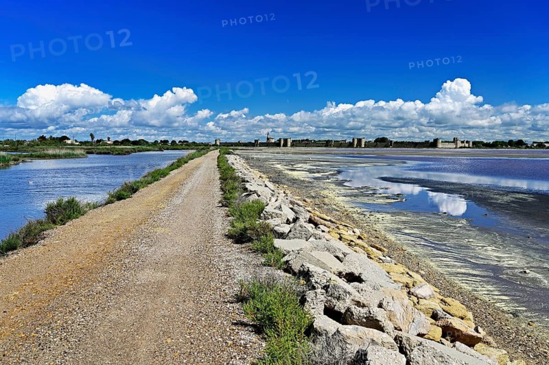 Extensive salt marshes of the Salins du Midi criss-crossed by canals and roads, the historic city wall in the back, Aigues-Mortes, Camargue, southern France, France