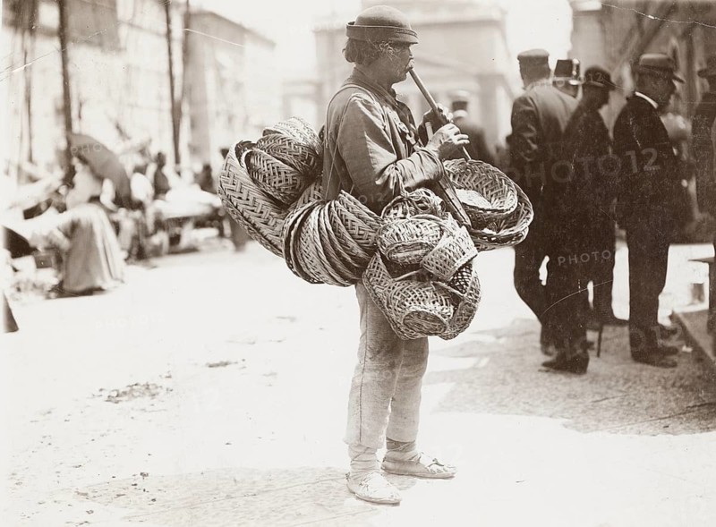Slovakian, flying merchant, ambulatory business, baskets, flute playing, poverty, A man carrying many baskets and playing a wind instrument in a busy street, Philipp Kester, around 1906