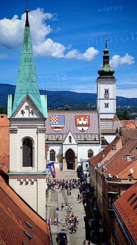 View from Lotrscak Tower over a picturesque town with red tile roofs and a large church with painted roof under a blue sky, Zagreb, Croatia