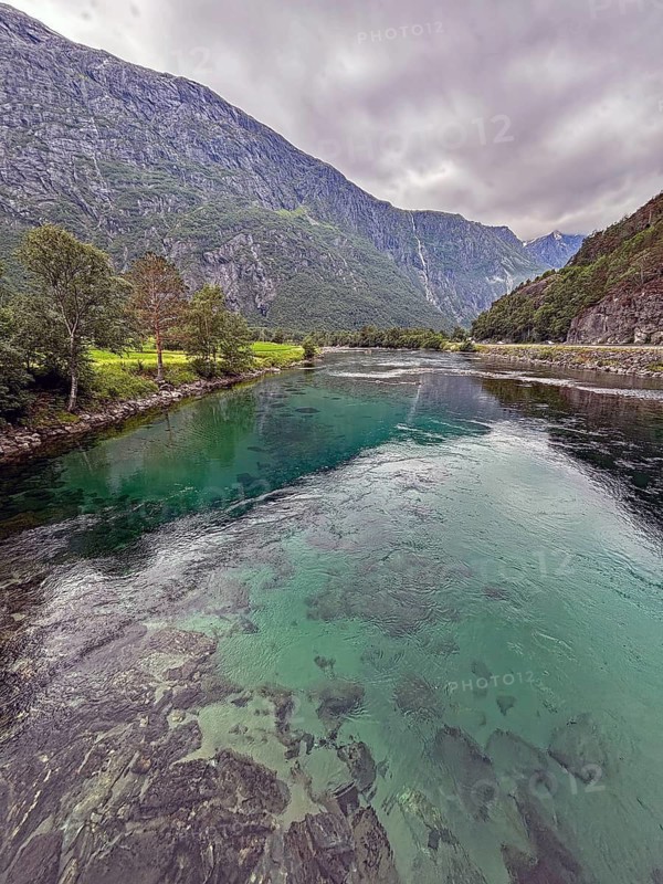 A clear river flows through a mountainous landscape under a cloudy sky, Raumadalen, Trollvegen, Andalsnes, Norway
