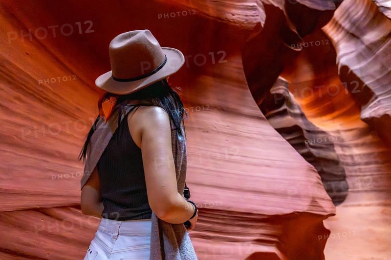 Woman wearing a hat admiring the unique geological formations and vibrant colors inside the slot canyon, enjoying a travel adventure and discovering the beauty of nature