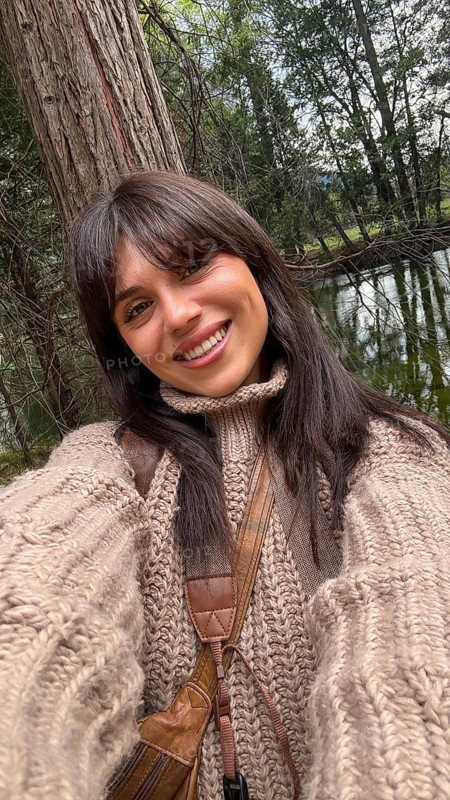 Young woman smiling, enjoying outdoors in nature, standing near a tree and river in yosemite national park while wearing a knitted sweater, embodying natural beauty, freedom, and happiness