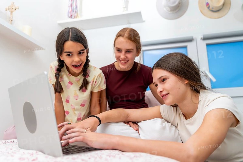 Three young girls are sharing a cheerful moment, watching a laptop together in a bright room, experiencing surprise and togetherness, sharing connections and enjoying education or entertainment