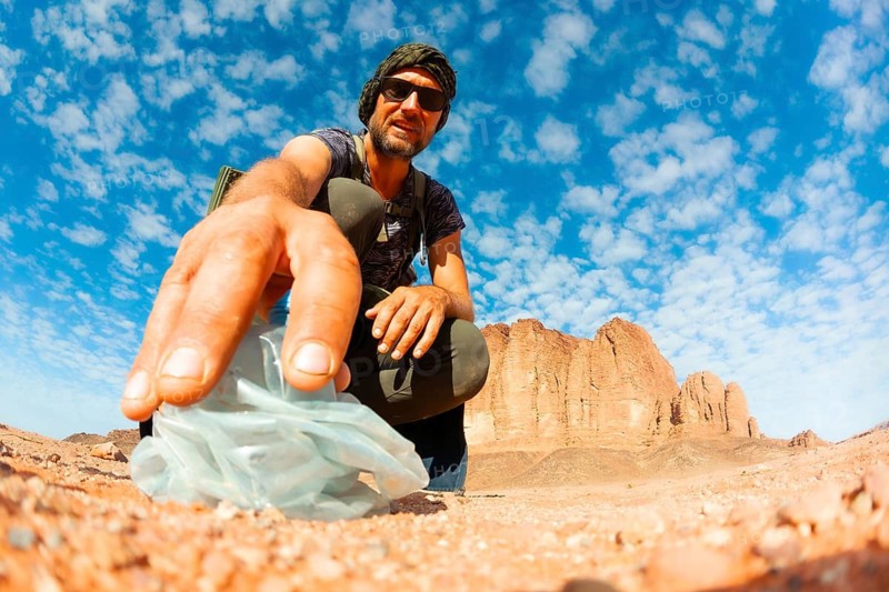 Environmental hiker picks up old plastic bottle waste in Wadi Rum desert, Jordan. A powerful scene highlighting sustainability, conservation, and individual action for Earth Day awareness.Jordan trail